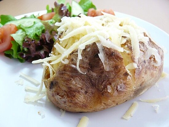 Golden-brown baked potato with melted cheese and a fresh salad on a clean white plate.