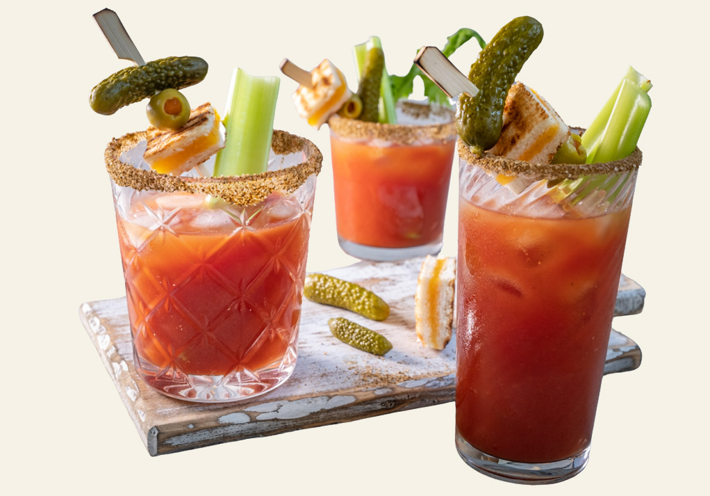 Vibrant Bloody Mary cocktails with garnishes served in elegant glassware on a wooden tray.