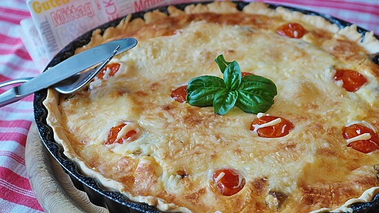 Cheesy tomato pie with basil on a rustic board, perfect for a hearty lunch.