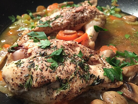 Golden-brown chicken with colorful vegetables in a rustic sauté pan, garnished with fresh herbs.