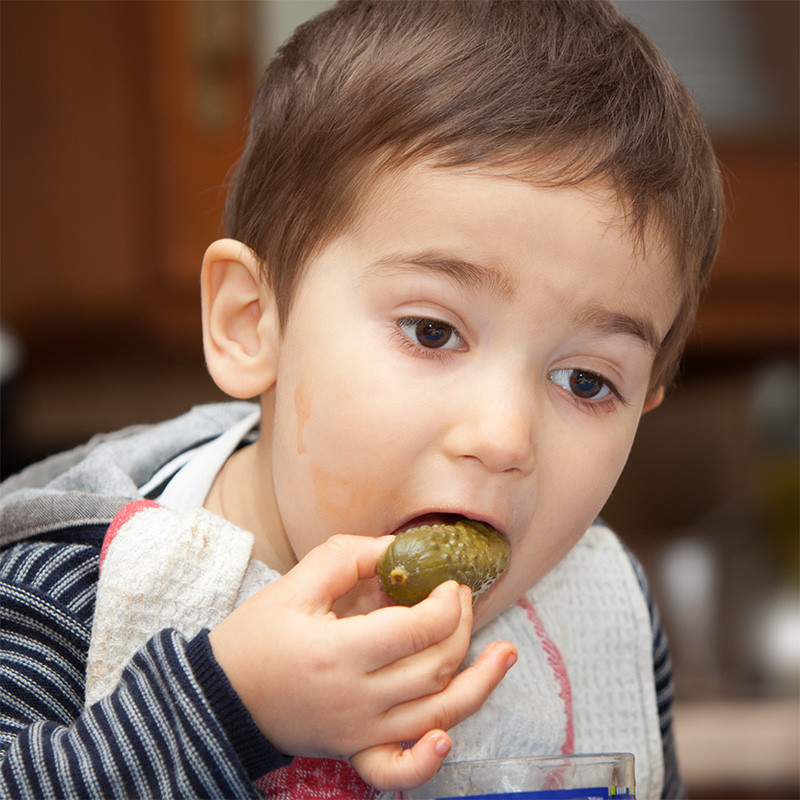 Young boy enjoying a pickle in a cozy kitchen, capturing joyful childhood moments.