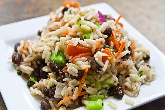 Colorful rice and bean salad with fresh vegetables on a clean white plate.