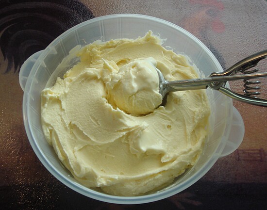 Rich creamy dairy treat in a clear container with an ice cream scoop, perfect for indulgence.