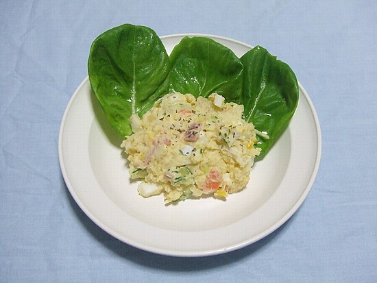 Creamy potato salad with fresh greens on a white plate against a soft blue background.