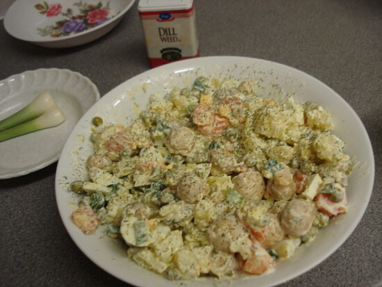 Colorful creamy seafood salad with dill, potatoes, shrimp, and veggies in a white bowl.