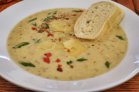 Creamy yellow soup garnished with herbs and cheese, served with crusty bread on a wooden table.