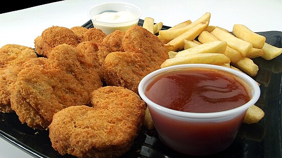 Heart-shaped chicken nuggets and golden fries with ranch and ketchup on a black plate.