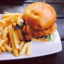 Crispy chicken sandwich with lettuce and tomato, served with golden french fries on a white plate.