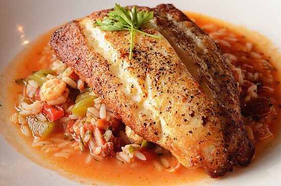 Perfectly cooked golden-brown fish fillet served over orzo pasta with shrimp and vegetables.