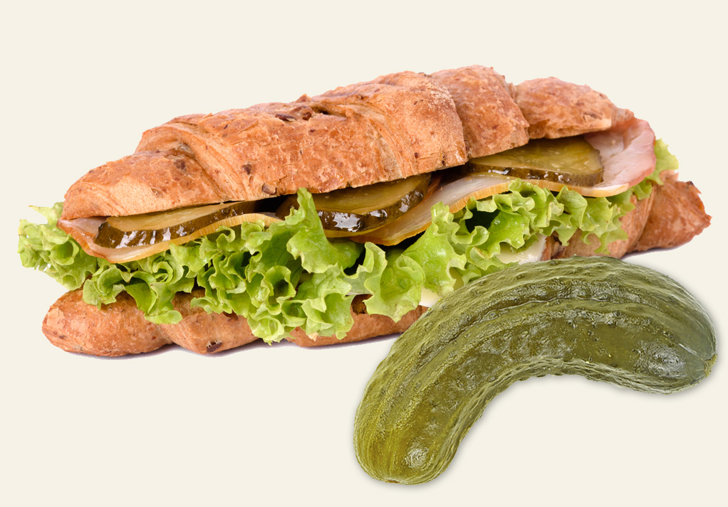 Croissant sandwich with pickles, lettuce, and deli meat, showcasing delicious textures and flavors.