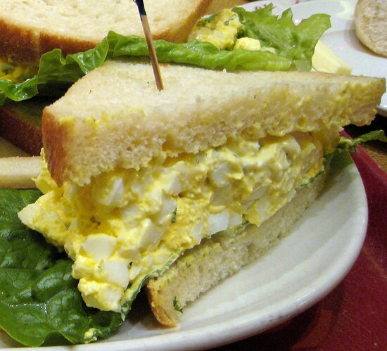 Toasted egg salad sandwich with fresh lettuce on a white plate. Perfect for lunch!