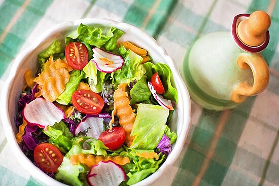 Fresh salad with greens, cherry tomatoes, radishes, and carrots in a ceramic bowl.