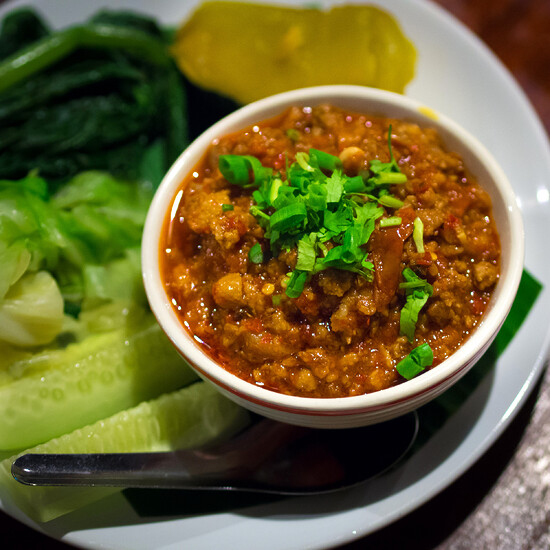 Colorful vegetable platter with vibrant chili sauce, fresh herbs, cucumbers, and tangy pickles.