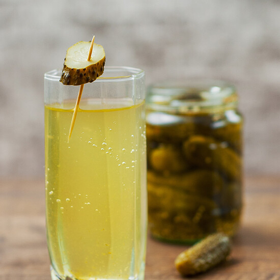 Refreshing golden-yellow drink garnished with a pickle slice, perfect for summer gatherings.