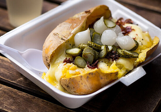 Gourmet baked potato topped with melted cheese, pickles, bacon bits, and pearl onions.