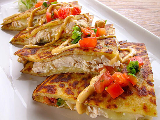 Golden grilled chicken quesadillas topped with fresh tomatoes, cilantro, and creamy sauce on a rustic plate.