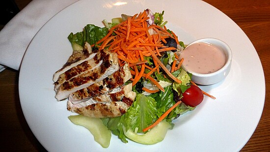 Vibrant grilled chicken salad topped with fresh vegetables and creamy dressing on a white plate.