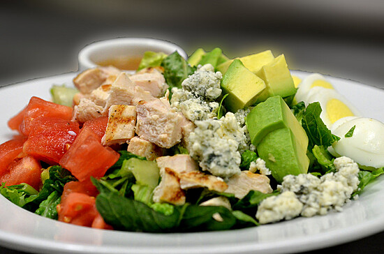 Colorful grilled chicken salad topped with fresh vegetables, avocado, blue cheese, and hard-boiled eggs.