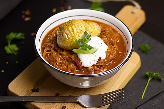 Delicious cabbage stew topped with sour cream and parsley, served on a rustic cutting board.