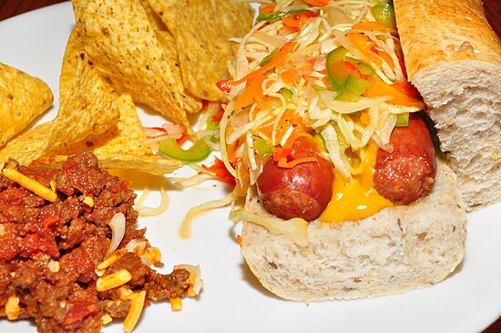 Delicious hot dog with chili and tortilla chips, topped with fresh veggies and melted cheese.