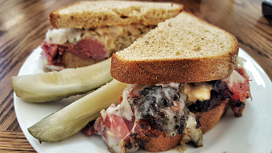 Hearty rye sandwich with corned beef and dill pickles on a rustic wooden table.