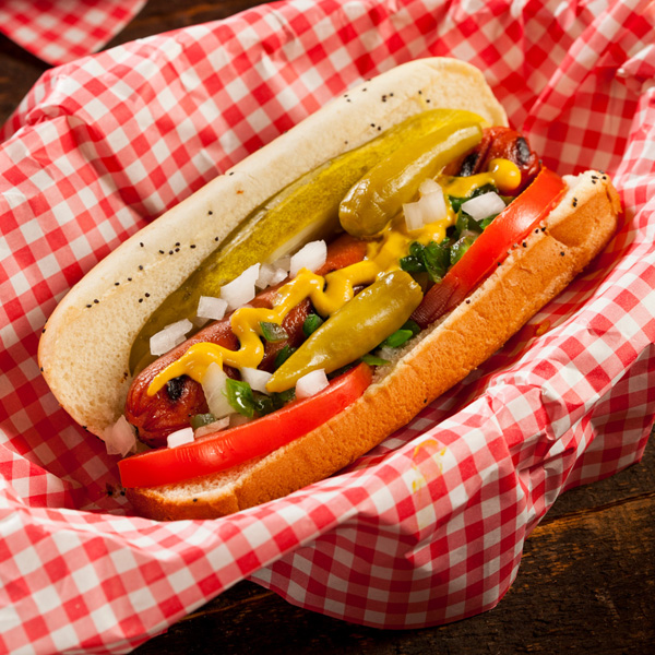 Delicious hot dog topped with fresh ingredients in a rustic red and white liner.