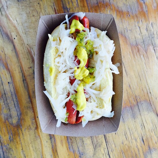 Classic hot dog with sauerkraut, mustard, and relish in a rustic cardboard tray.