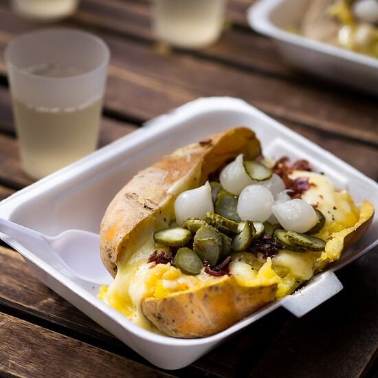 Loaded baked potato topped with creamy cheese, pickles, and onions in a cozy dining setting.