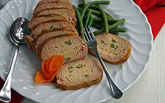 Sliced meatloaf with green beans and a carrot flower garnish on a white plate.