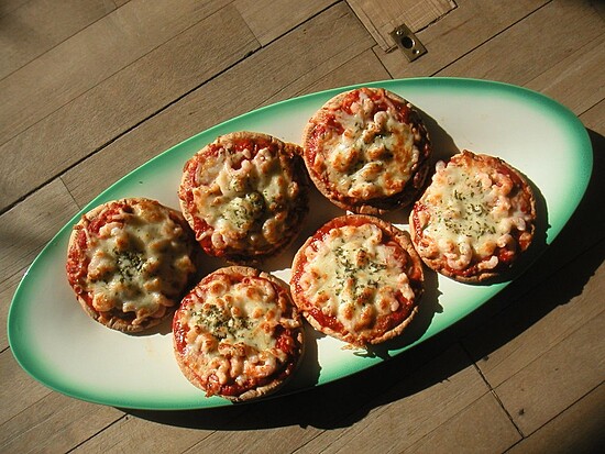 Mini pizzas on a green platter, topped with golden cheese and fresh herbs for sharing delight.