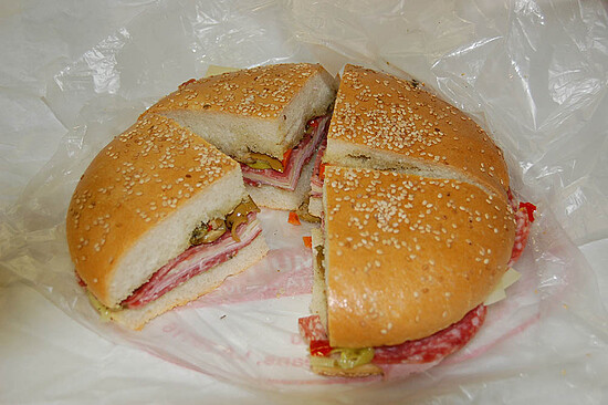 Delicious New Orleans Muffaletta filled with meats, cheese, and colorful vegetables on toasted sesame roll.