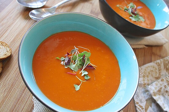 Elegant orange soup bowls with microgreens on a rustic wooden table, perfect for cozy meals.