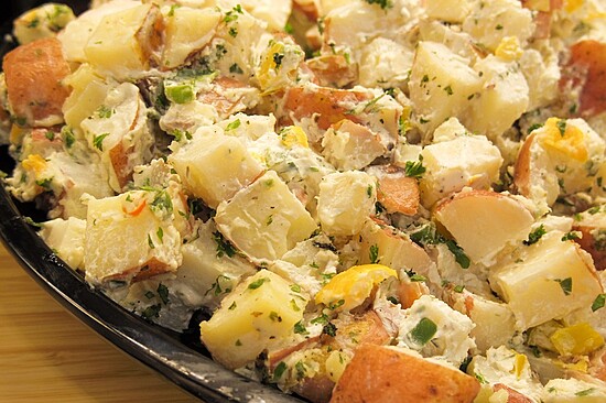 Creamy potato salad with fresh vegetables served in a stylish black dish for gatherings.