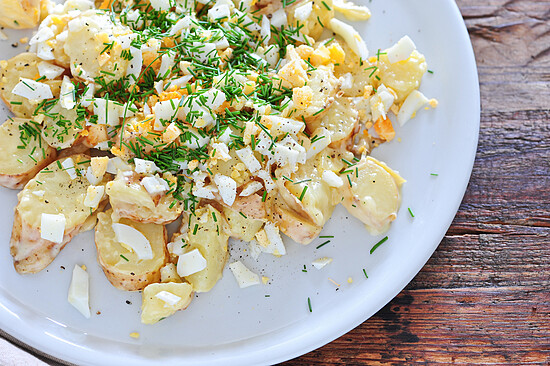 Vibrant potato salad with chives, hard-boiled eggs, and a creamy dressing on a rustic plate.