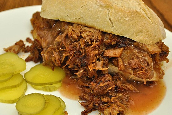 Savory pulled pork sandwich with tangy pickles on a rustic wooden surface.