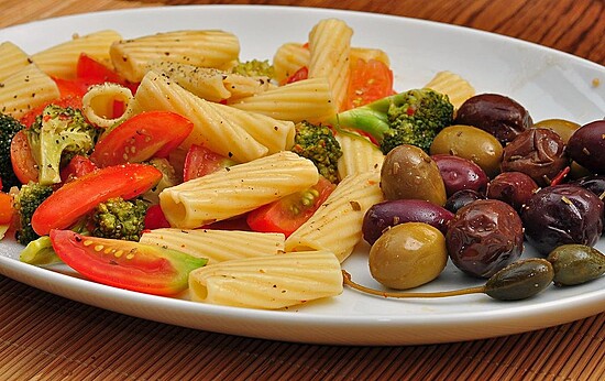 Delicious rigatoni salad with broccoli, tomatoes, olives, and bell peppers on a rustic wood background.