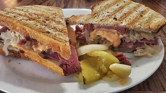 Toasted corned beef sandwich with sauerkraut and pickles on a rustic plate.