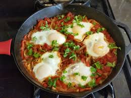 Sizzling cast-iron skillet eggs with sautéed tomatoes and fresh herbs for a comforting breakfast.