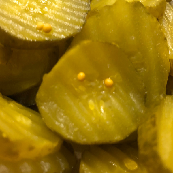 Close-up of vibrant green sliced pickles with glossy texture and yellow seeds.