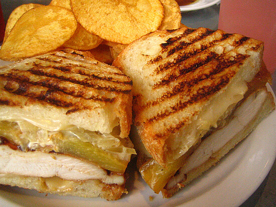 Toasted chicken sandwich with melted cheese and crispy chips for a satisfying meal experience.