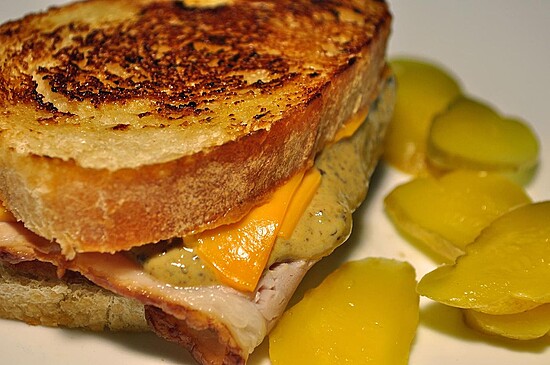 Toasted sandwich with melted cheddar, turkey, zesty mustard, and fresh pickles on a plate.