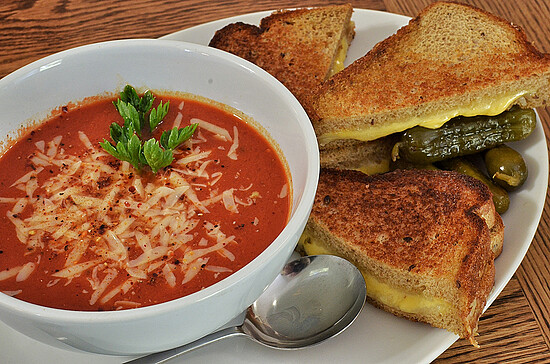 Classic tomato soup and grilled cheese sandwiches, with pickles, on a rustic wooden table.