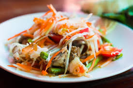 Colorful spicy chicken salad with shredded vegetables and chili peppers on a white plate.