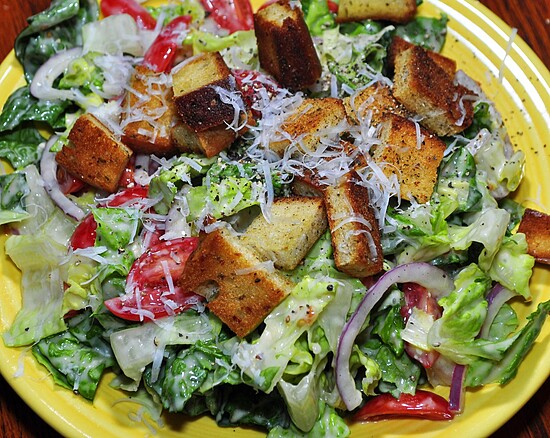 Colorful salad with croutons and Parmesan cheese on a bright yellow plate.